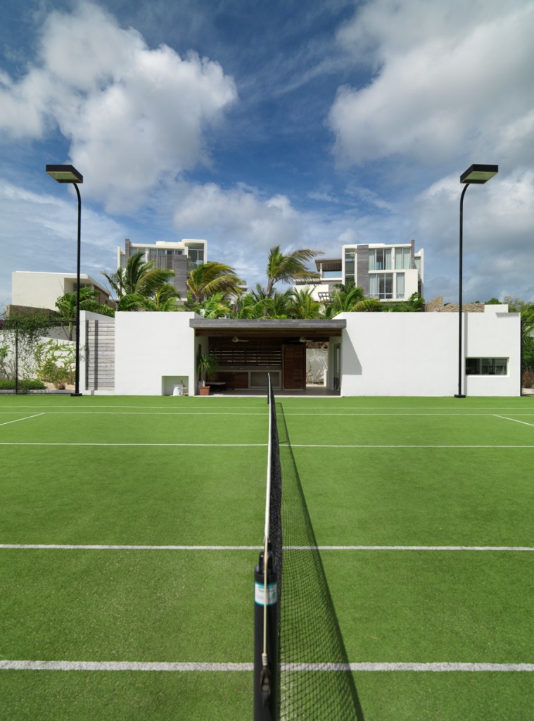 The illuminated tennis courts and gym with the villas above in the background